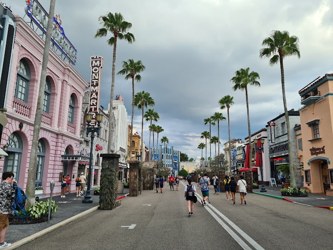 A sunny street lined with palm trees, people walking down the sidewalk.