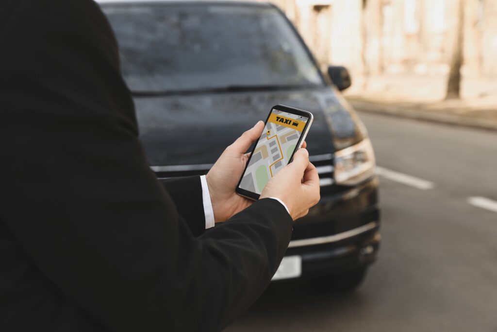 Man in formal attire holding cellphone by dark vehicle.