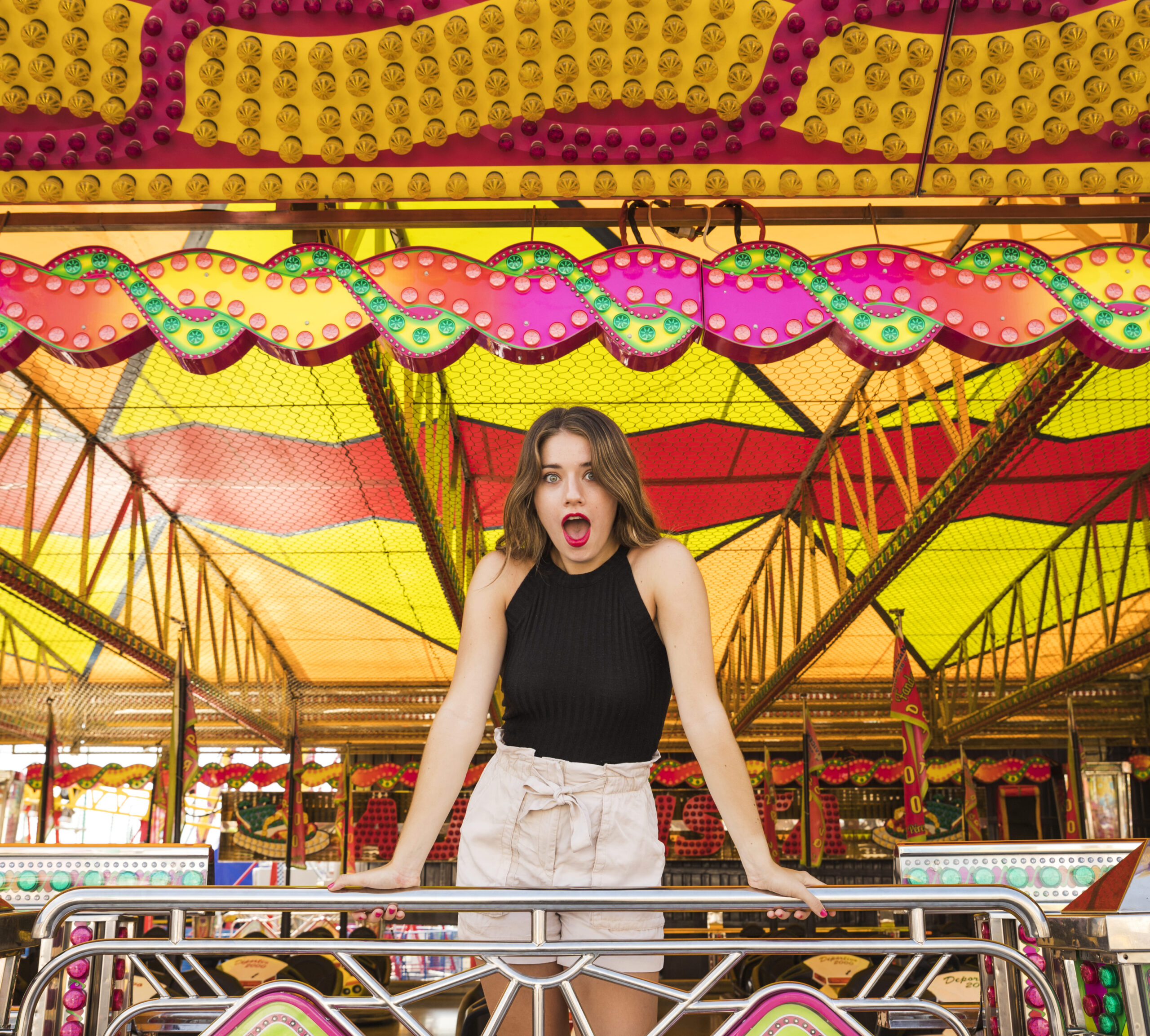 Woman standing on carousel, smiling, with colorful lights in background.