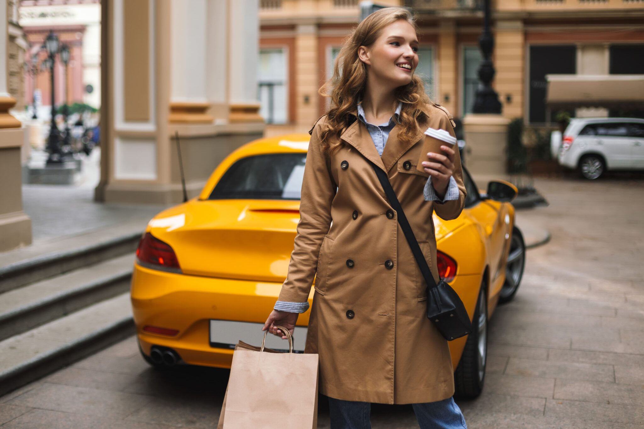 Woman in trench coat holding coffee cup near yellow car.